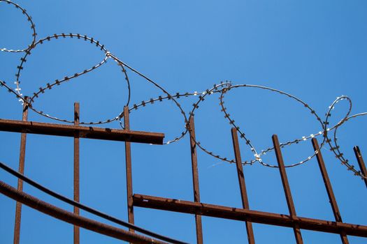 Enlightened barbed wire on the top of a metal fence. Bright blue sky in the background.