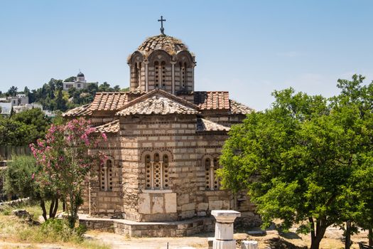 Old orthodox basilica in the city center of Athens. Park with olive and oleander trees. Hill in the background. Blue sky.