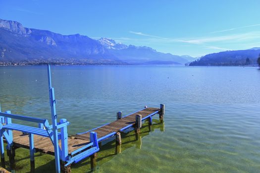 Blue wooden pontoon on Annecy lake and Alps mountains by beautiful day, France