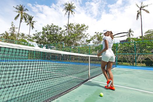 Beautiful young woman on tennis court of tropical resort
