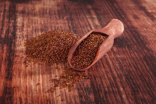 Red quinoa seeds on wooden scoop on wooden table. Healthy eating.