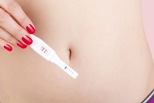 Sexy woman with red nails holding pregnancy test against her belly. Maternity and pregnancy test.