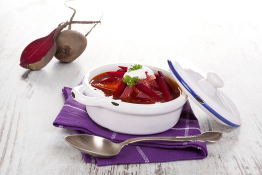 Delicious ukrainian borsch soup with fresh beetroot vegetable on purple cloth on rustic wooden table. Traditional european cuisine.