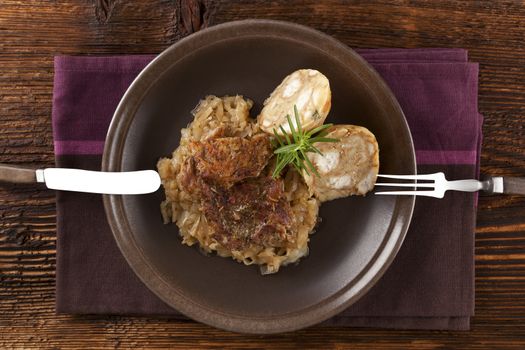 Baked pork chop with dumplings and sauerkraut on plate with silver cutlery on wooden table, top view. 