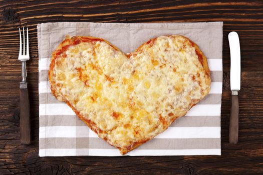 Delicious pizza in heart shape on wooden table, top view. Culinary pizza eating. I love pizza.