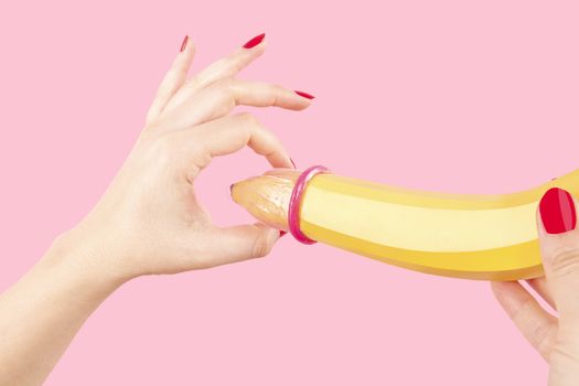 Female hand with red fingernails puts on a condom onto a banana. Safe sex concept.