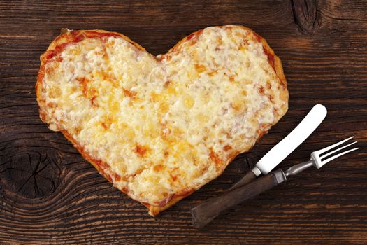 Delicious pizza in heart shape on wooden table, top view. Culinary pizza eating. I love pizza.