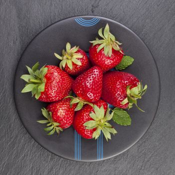 Delicious ripe strawberries on black plate on black stone, flat lay. Healthy fruit eating.
