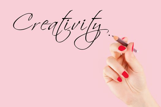 Creative industries. Female hand with pencil writing the word creativity in caligraphy.