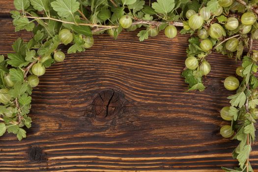 Green gooseberries with green leaves on wooden vintage table, top view. Healthy summer fruit eating. 