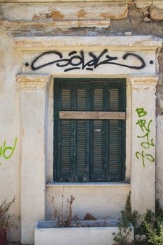 Abandoned house in the Plaka district of Athens. Green wooden shutter, old yellow facade with several graffiti tags.