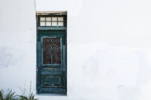 Old blue door with ornamental grille. White facade of the house. Few plants in the corner. Plaka district of Athens, Greece.