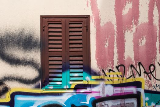 Neutral basic color of the facade of the house. Window covered with brown shutter. Many colorful graffiti tags. Plaka district of Athens, Greece.