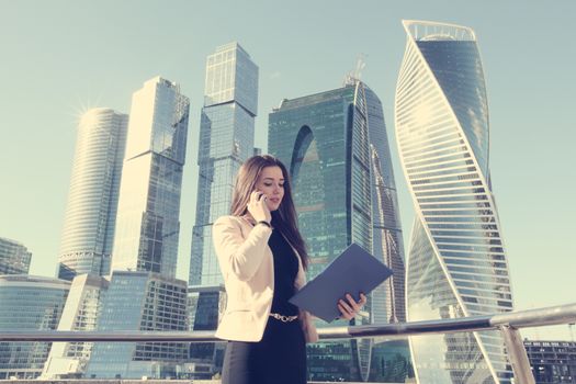 Young beautiful businesswoman with cellphone outdoors at skyscraper background