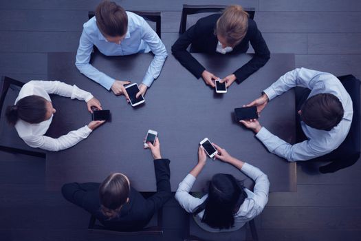 Business people with smartphones sitting around the table, top view