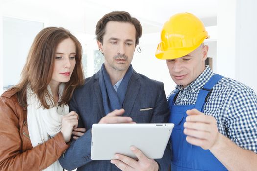 Worker and couple using tablet pc at construction site