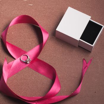 A diamond ring on a pink ribbon white jewelry box