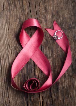 Beautiful pink ribbon with a ring on a wood background, greetings on happy women's day