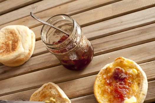 Freshly toasted crumpets with jam served for breakfast on an outdoor slatted wooden garden table