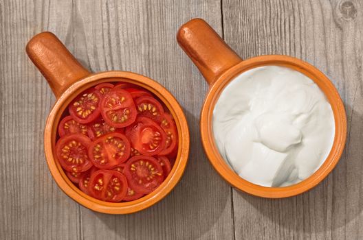 Chopped tomatoes and sour cream in a ceramic bowl on old wooden surface.