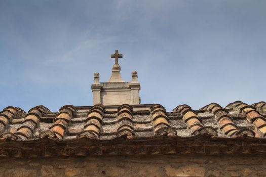 Old tiled roof. Small tower with a cross. Blue sky with clouds.