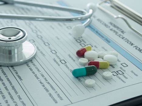 pill with stethoscope , medical record application form on physicians desk