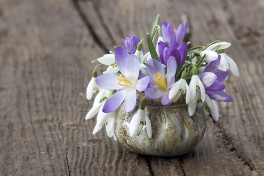 Bunch of crocus and snowdrops in a vase on the wooden table.