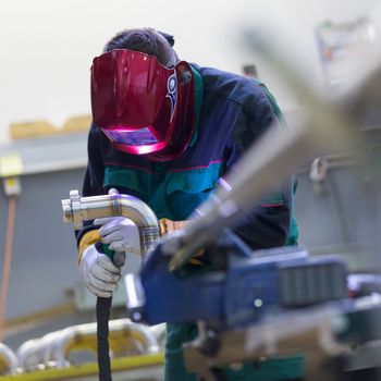 Industrial worker with protective mask welding inox elements in steel structures manufacture workshop.