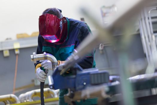 Industrial worker with protective mask welding inox elements in steel structures manufacture workshop.