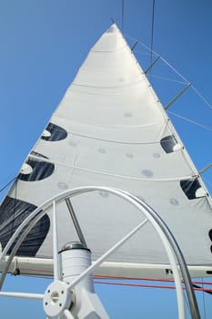 The mast, sail and rudder of the yacht on the background of blue sky