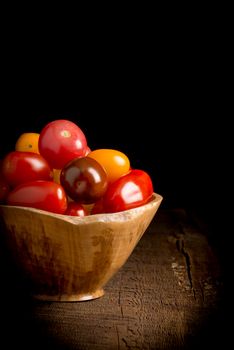 Bowl of colorful organic tomatoes on a low key rustic background.  Suitable for food industry promotional material.