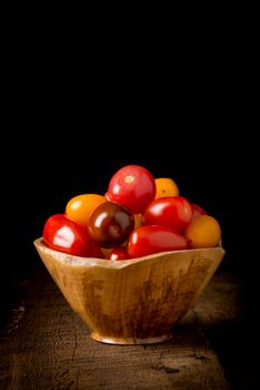 Bowl of fresh heirloom tomatoes on a low key rustic background.  May be suitable for food services promotional materials.
