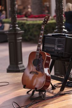 Six-string acoustic guitar sits on a stand on an outdoor stage, ready for a live music performance.