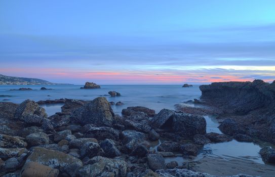 Long exposure of sunset over rocks, giving a mist like effect over ocean in Laguna Beach, California, United States