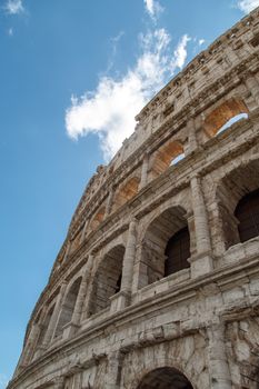 Bottom view of ancient amphitheatre of Colosseum built by Vespasian and Titus in Rome, on cloudy blue sky background.