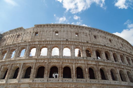Bottom view of ancient amphitheatre of Colosseum built by Vespasian and Titus in Rome, on cloudy blue sky background.