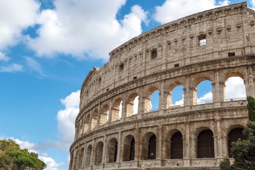 Close up detailed view of ancient amphitheatre of Colosseum built by Vespasian and Titus in Rome, on cloudy blue sky background.
