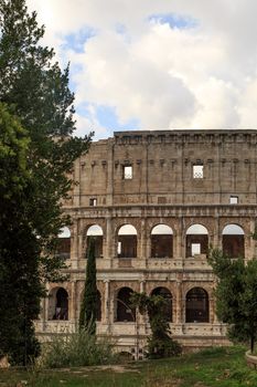 View of amphitheatre of Colosseum built by Vespasian and Titus in Rome, inside trees, on cloudy blue sky background.