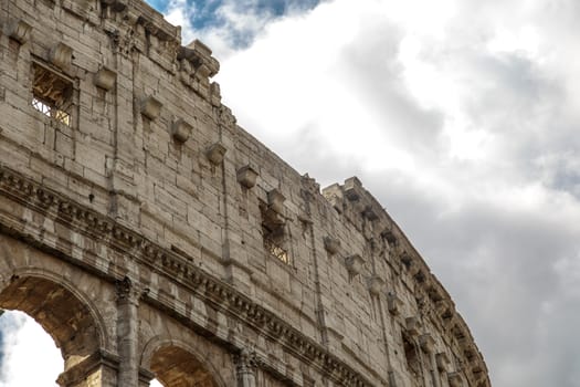 Close up detailed view of ancient amphitheatre of Colosseum built by Vespasian and Titus in Rome, on cloudy sky background.