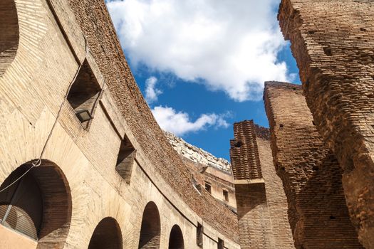 Close up detailed inside view of ancient amphitheatre of Colosseum built by Vespasian and Titus in Rome, on cloudy blue sky background.