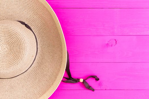 Wide-brimmed straw sunhat on vibrant exotic pink background with copy space conceptual of tropical vacations and travel viewed from above