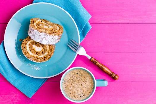 Top down view of two slices of roulo cake dessert and mug of coffee next to fork on napkin over light purple wooden table