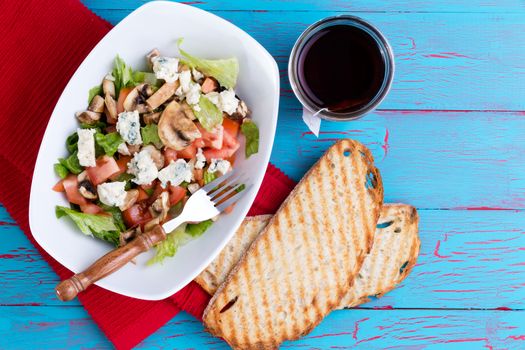 Healthy mixed salad with feta cheese served with tea and toast on an exotic bright turquoise blue picnic table with copy space, overhead view