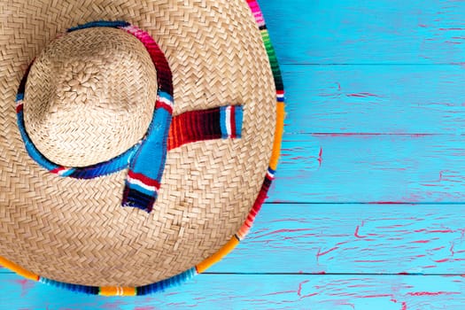 Colorful wide brimmed straw sombrero with multicolor trim and ribbon lying on a bright blue picnic table with copy space conceptual of summer travel