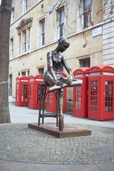 LONDON, UK - DECEMBER 20: Young Dancer statue, by Enzo Plazzotta, with line of red phone booths in the background. December 20, 2015 in London.