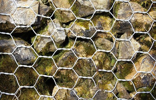 Closeup of a barrier built of small pieces of rock behind a fence of metallic mesh in thailand