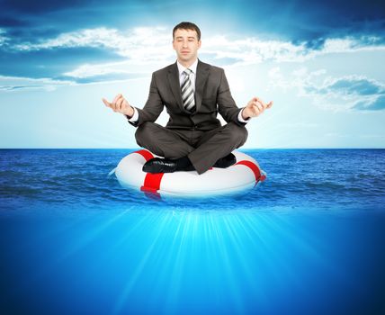 Buisnessman sitting in lotus posture on lifebuoy in sea, balance concept