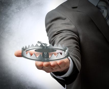 Businessman holding bear trap on grey wall background, danger concept