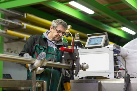 Industrial operator setting  computer controlled process of orbital welding machine in inox pipes manufacturing workshop.