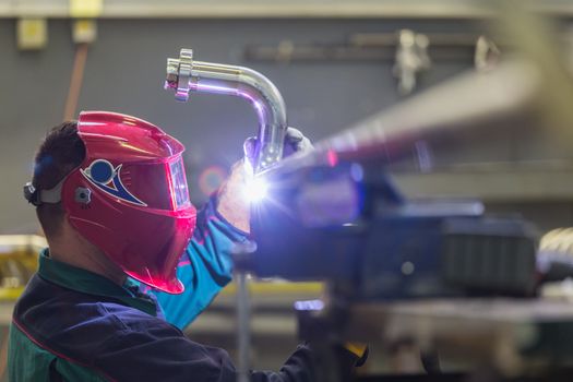 Industrial worker with protective mask welding inox elements in steel structures manufacture workshop.